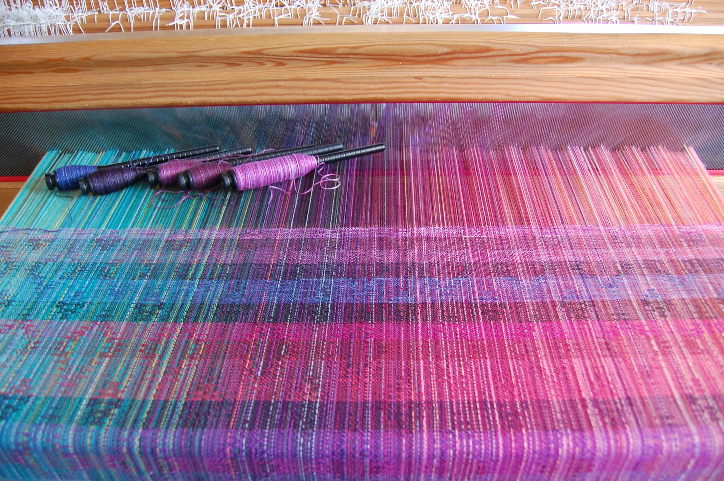 Variegated weft yarns (top five stripes). The bottom stripe corresponds with the left-most pern: 40% hemp/60% cotton in blues and purples, madeline tosh superwash lace merino in Clematis, 70% silk/30% sea cell in Amethyst, Phydeaux 80% superfine merino wool/20% silk in Pomegranate, 40% hemp/60% cotton in pinks and purples.
