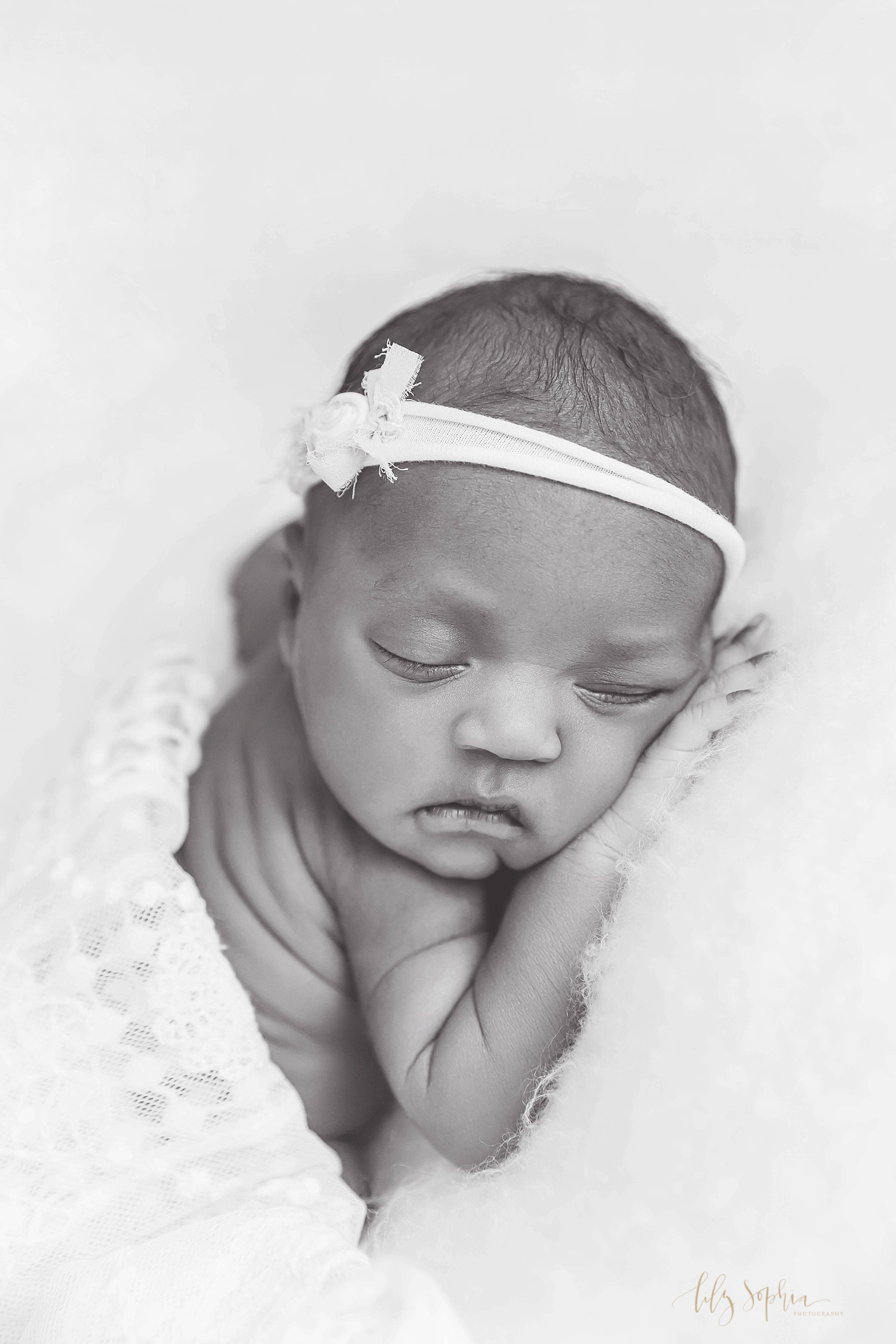  Black and white image of a sleeping, African American newborn girl, laying on her stomach, with a white bow in her hair.&nbsp; 