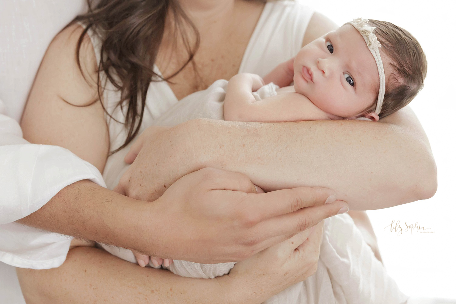  Close up image of a newborn, baby, girl in her mother and fathers arms, looking at the camera and pouting her lips.&nbsp; 