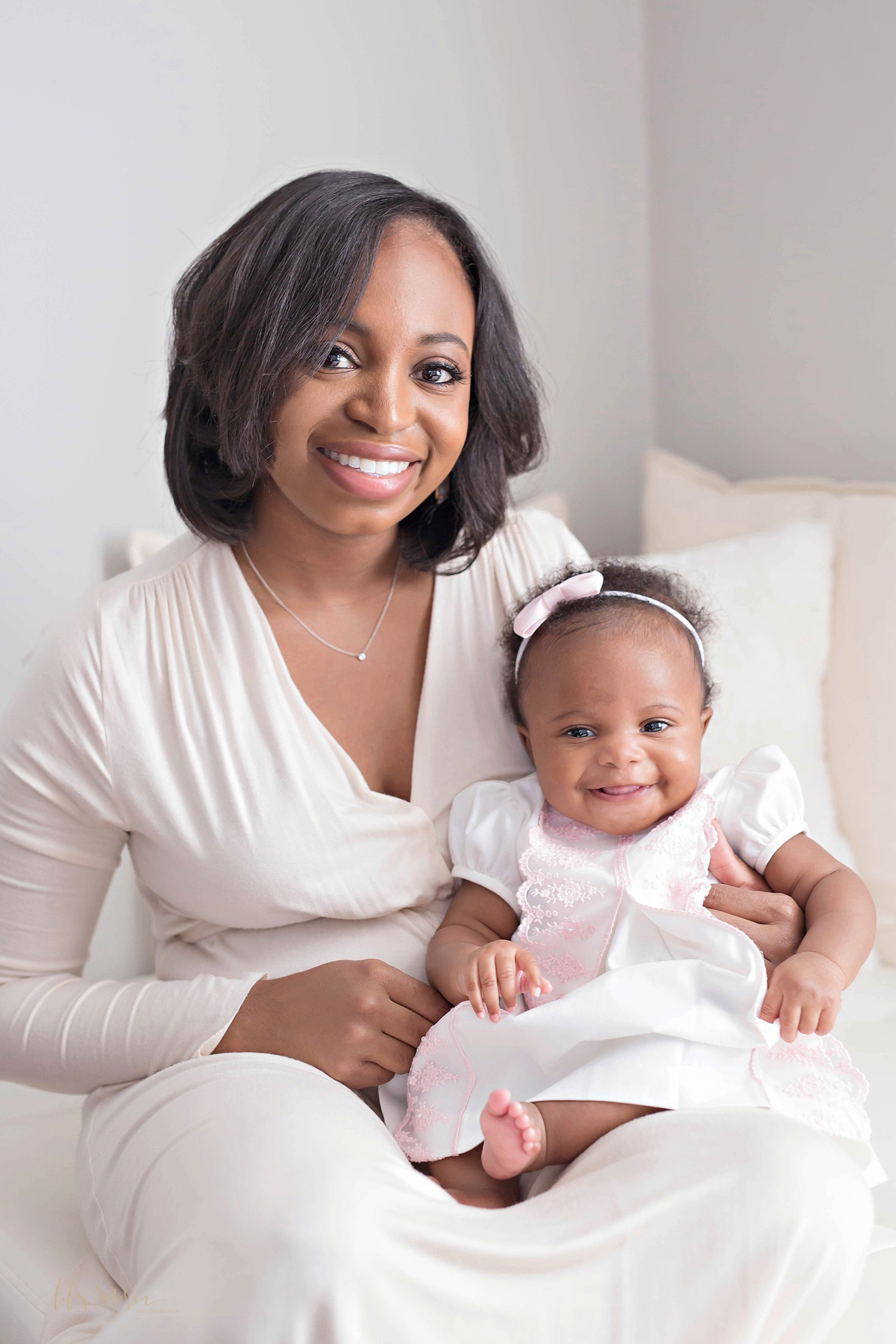  Image of an African American mother sitting on a bed and holding her smiling, three month old daughter, on her lap.&nbsp; 
