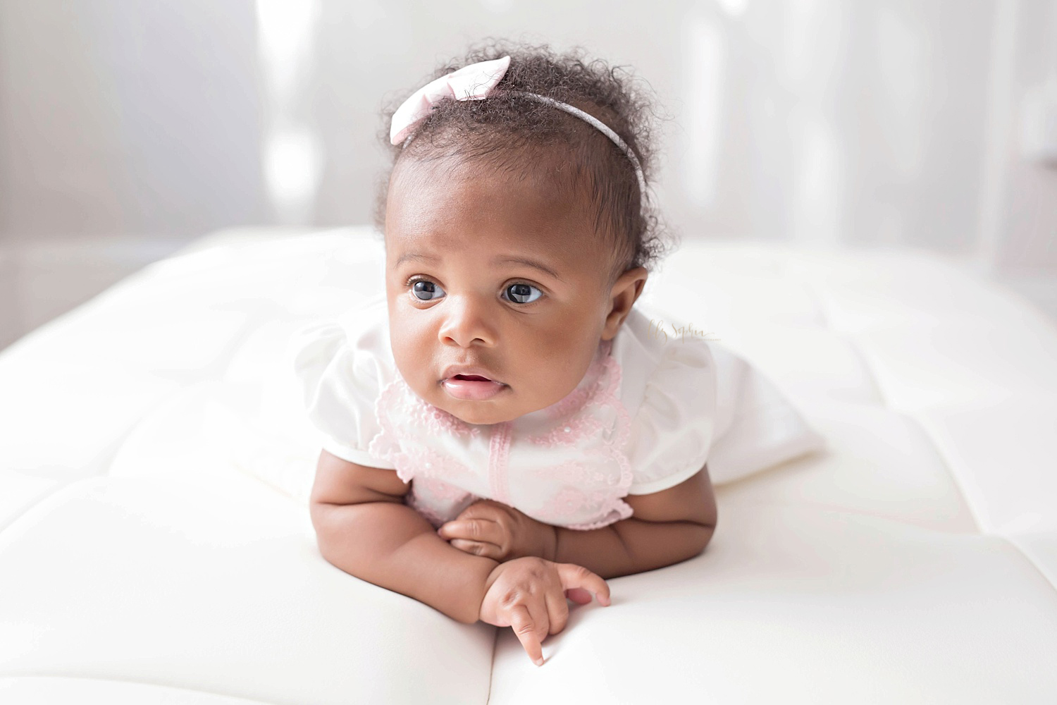  Image of an African American baby girl, laying on a bed and pushing up on her arms,&nbsp;&nbsp;and looking away from the camera.&nbsp; 