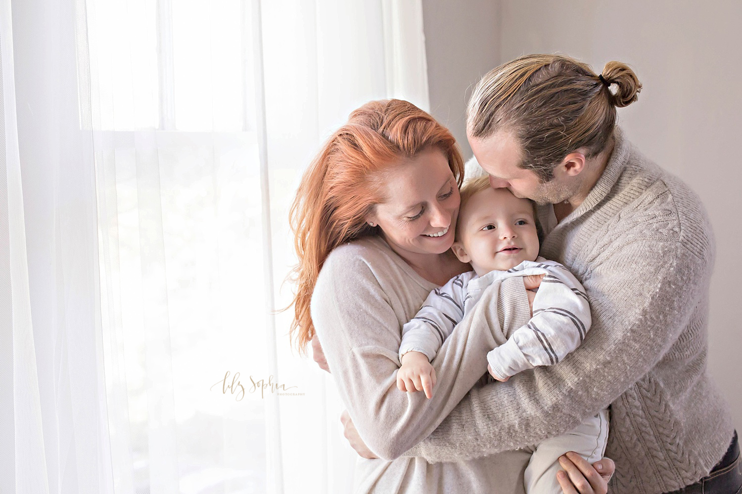  Image of a mother holding her son and smiling down at him, while his father hugs his wife and kisses his son's forehead.&nbsp; 