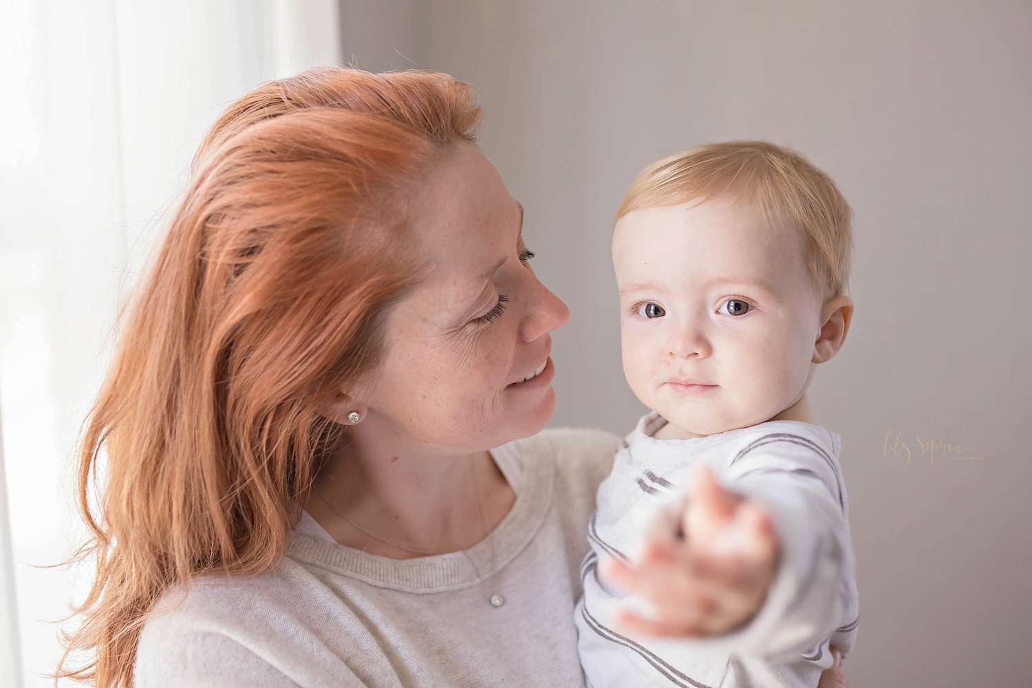  Image of a mother with red hair, holding her one year old son while he reaches for the camera.&nbsp; 