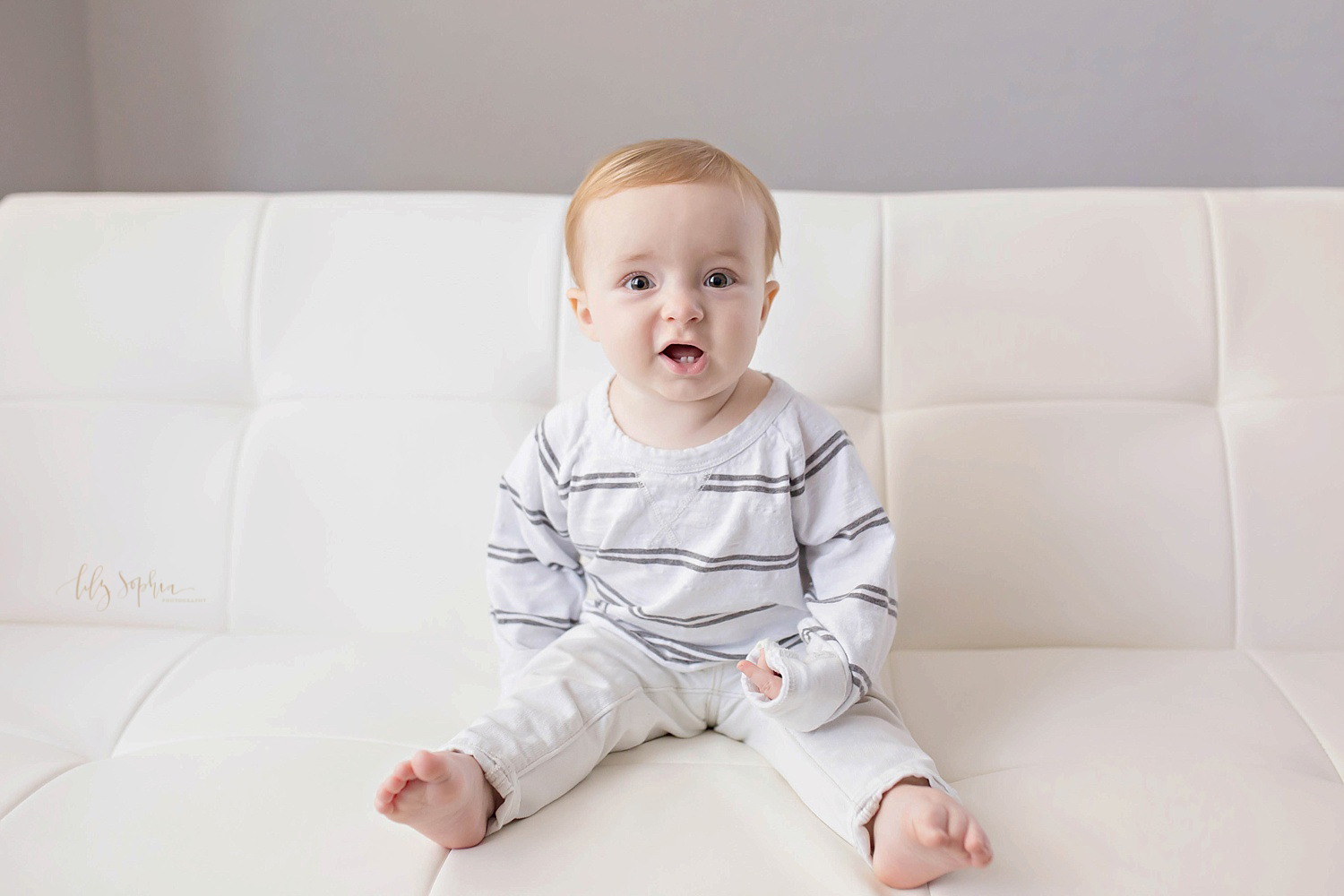  Image of a one year old boy, sitting on a couch, wearing khaki's and a striped shirt, and showing off his bottom two teeth.&nbsp; 