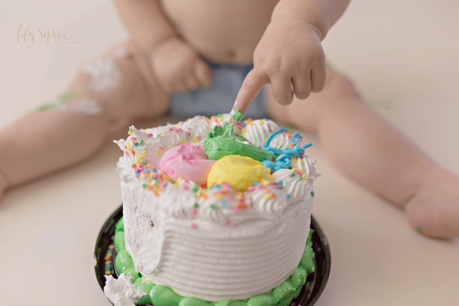  Image of a one year old baby boy, wearing a blue cloth diaper, and sticking his finger into the icing of his smash cake.&nbsp; 