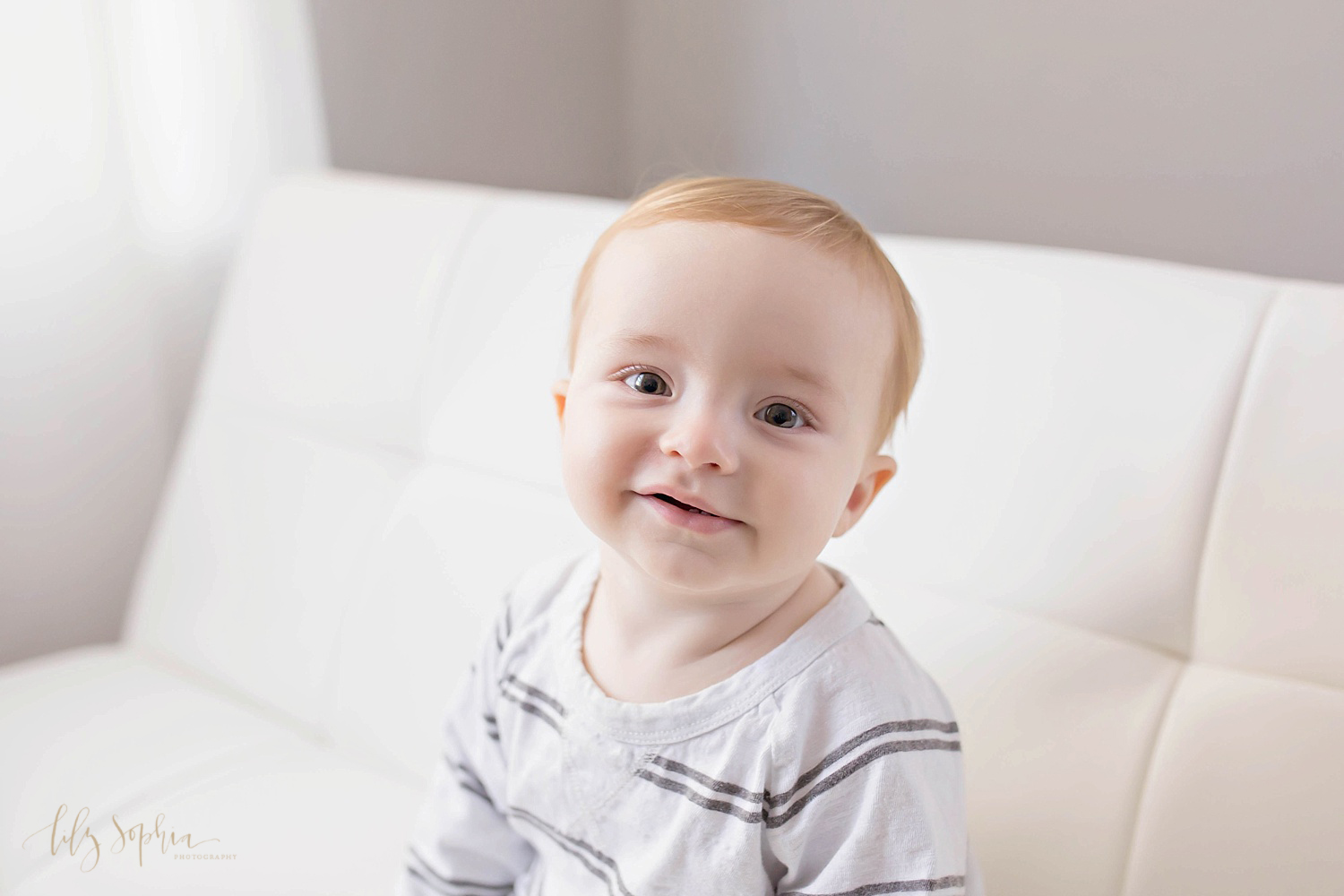  Image of a one year old boy, sitting on a couch and half smiling up at the camera.&nbsp; 