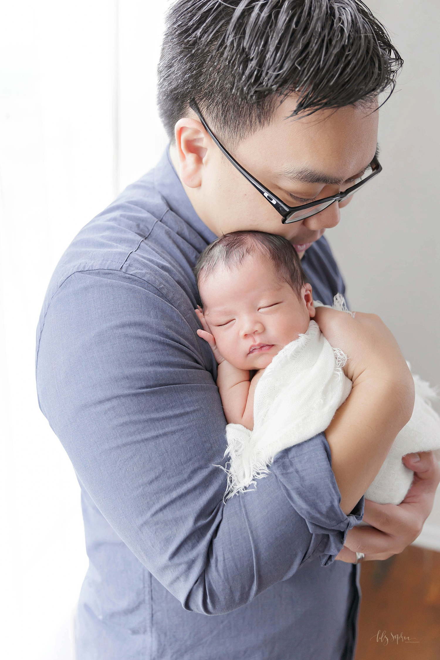  Image of an Asian man holding his sleeping newborn son against his shoulder. 