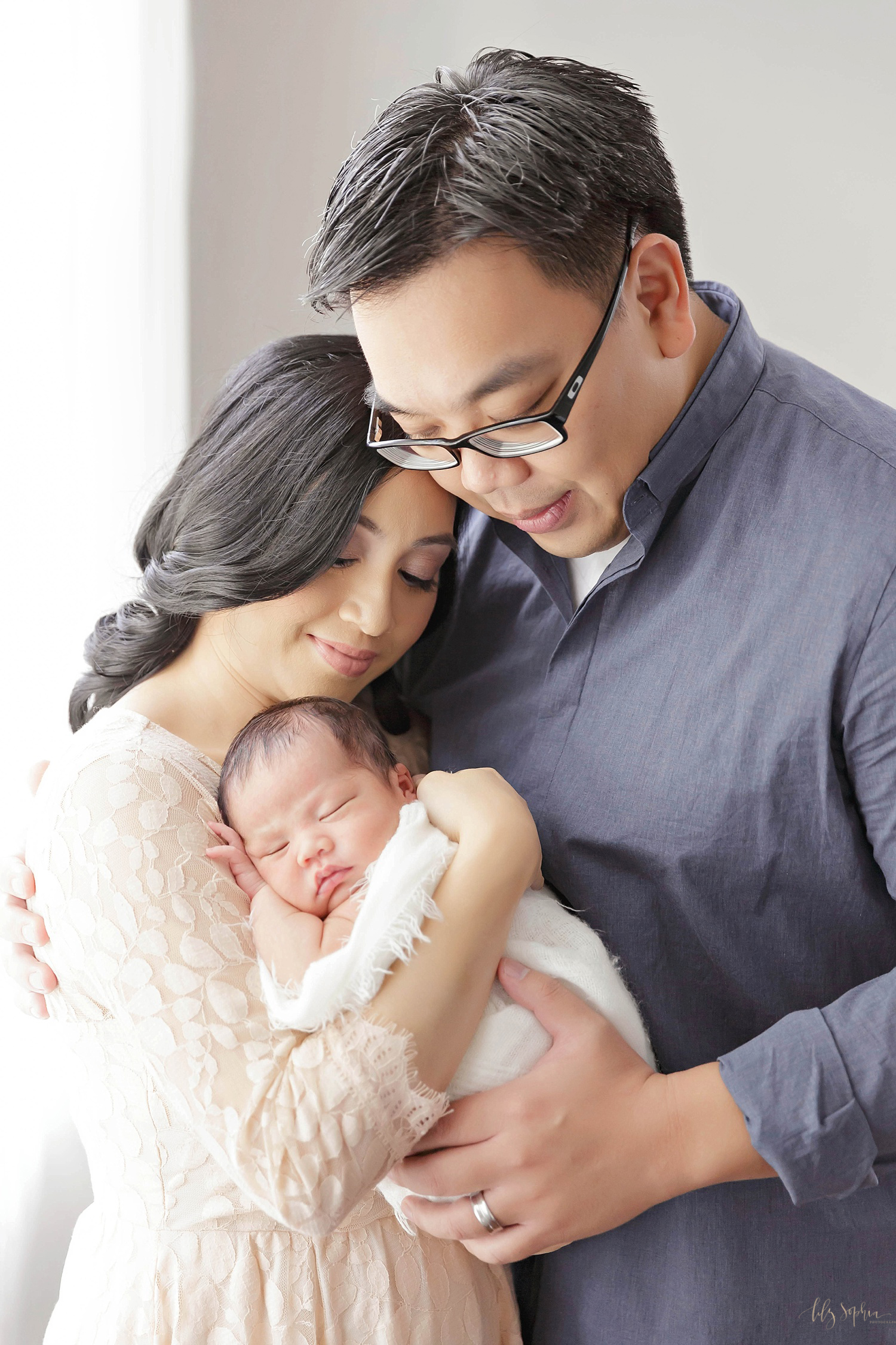  Filipino woman and Chinese man holding their sleeping newborn son, and looking down on him, smiling. &nbsp; 