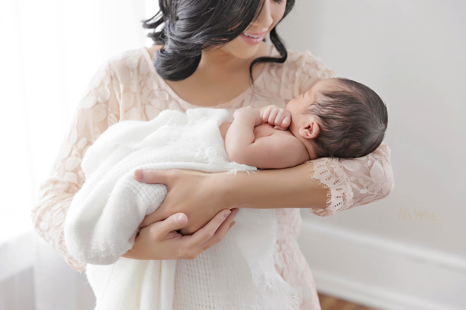  Image of a Filipino woman wearing a cream dress and cradling her sleeping newborn son, taken in the natural light studio of Lily Sophia Photography.&nbsp; 