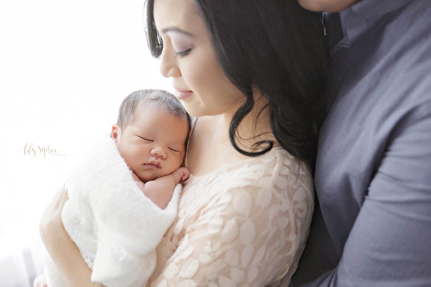  Asian woman holding her sleeping newborn son with her husband standing behind her. 