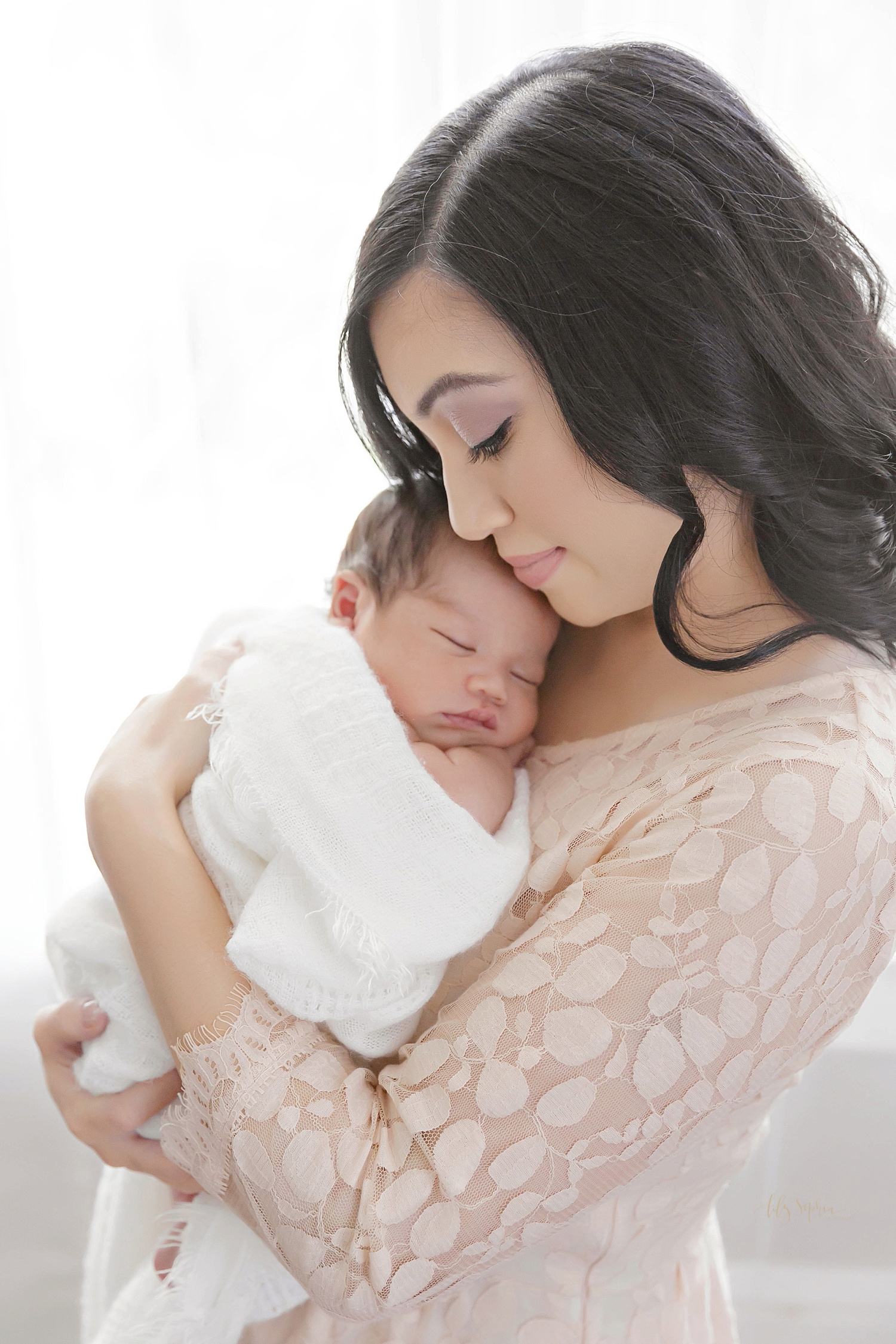  Asian woman holding her sleeping newborn son in her arms, taken at the natural light studio of Lily Sophia Photography. 