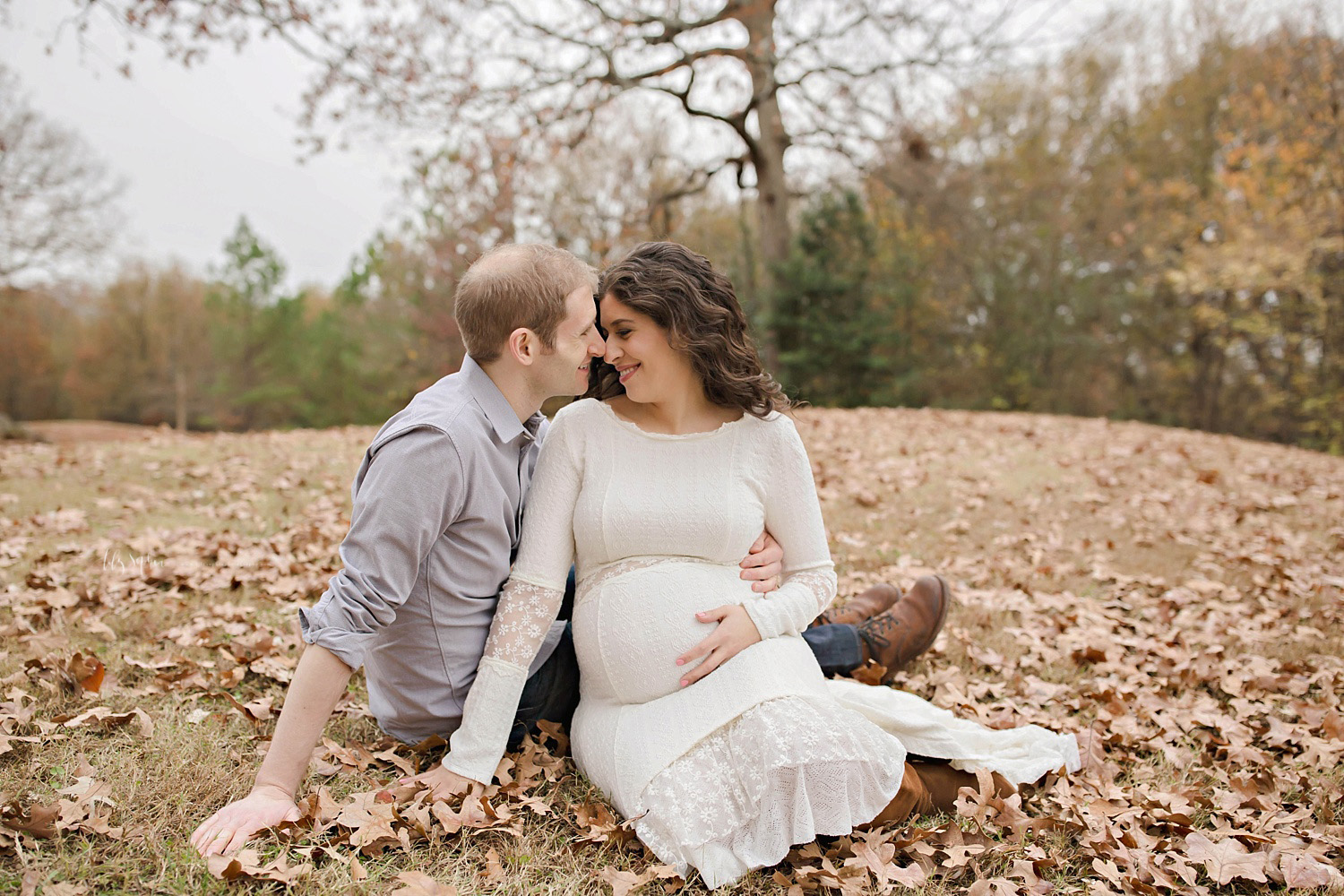 Atlanta couple expecting baby girl sitting on ground covered with leaves