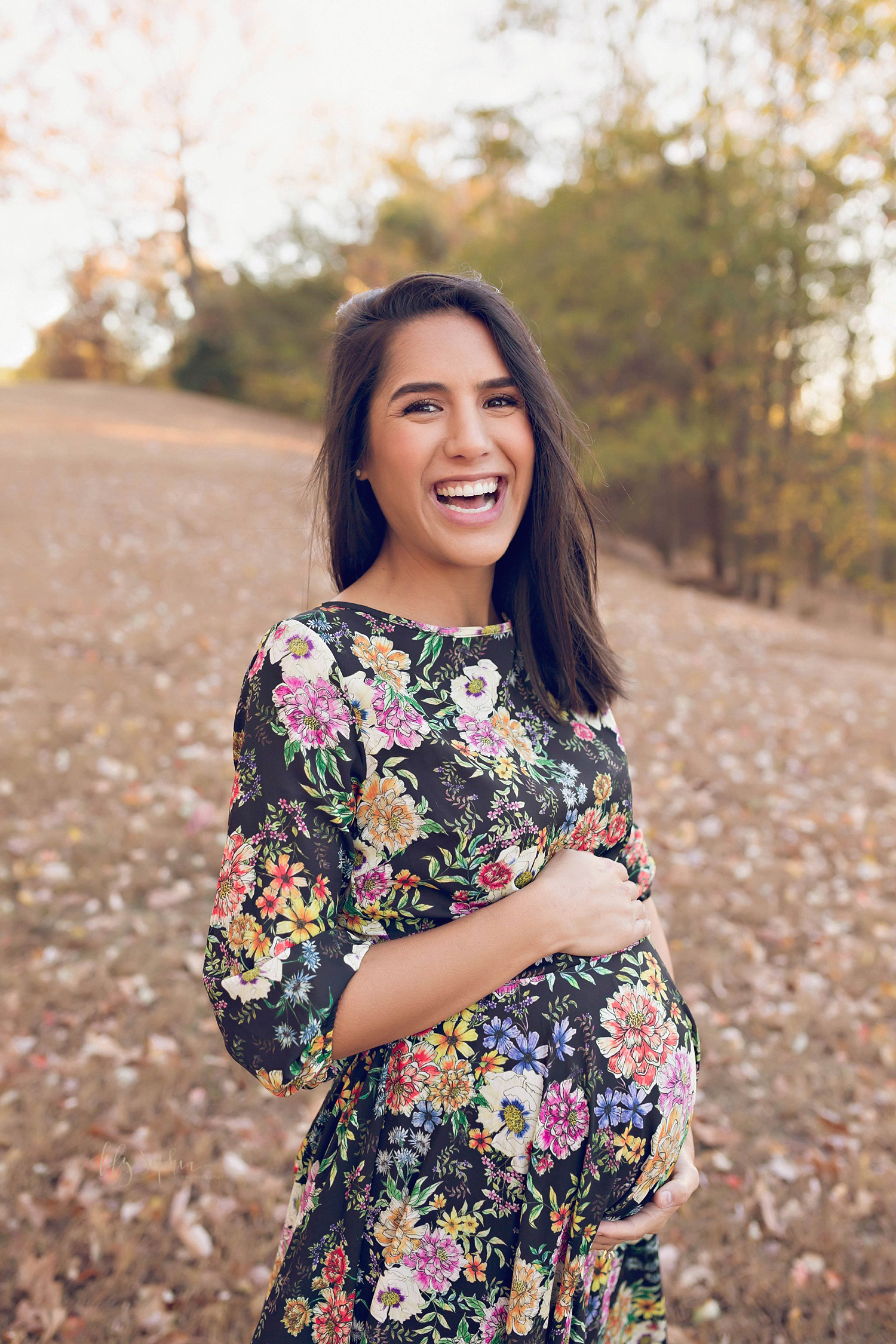  Pregnant woman wearing a floral dress smiling and laughing in a local Atlanta park.&nbsp; 