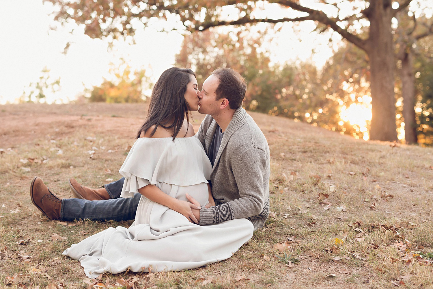  Pregnant woman wearing an off the shoulder dress sitting on the ground facing her husband with the sun setting behind them in Atlanta.&nbsp; 