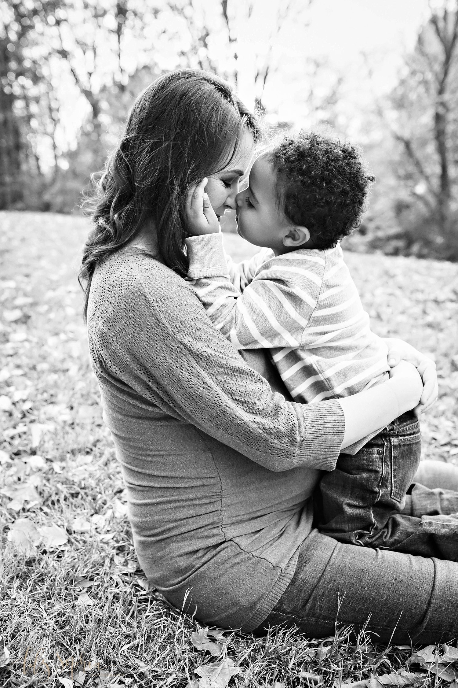  Image of a pregnant woman sitting down on the ground holding her son and giving him Eskimo kisses.&nbsp; 