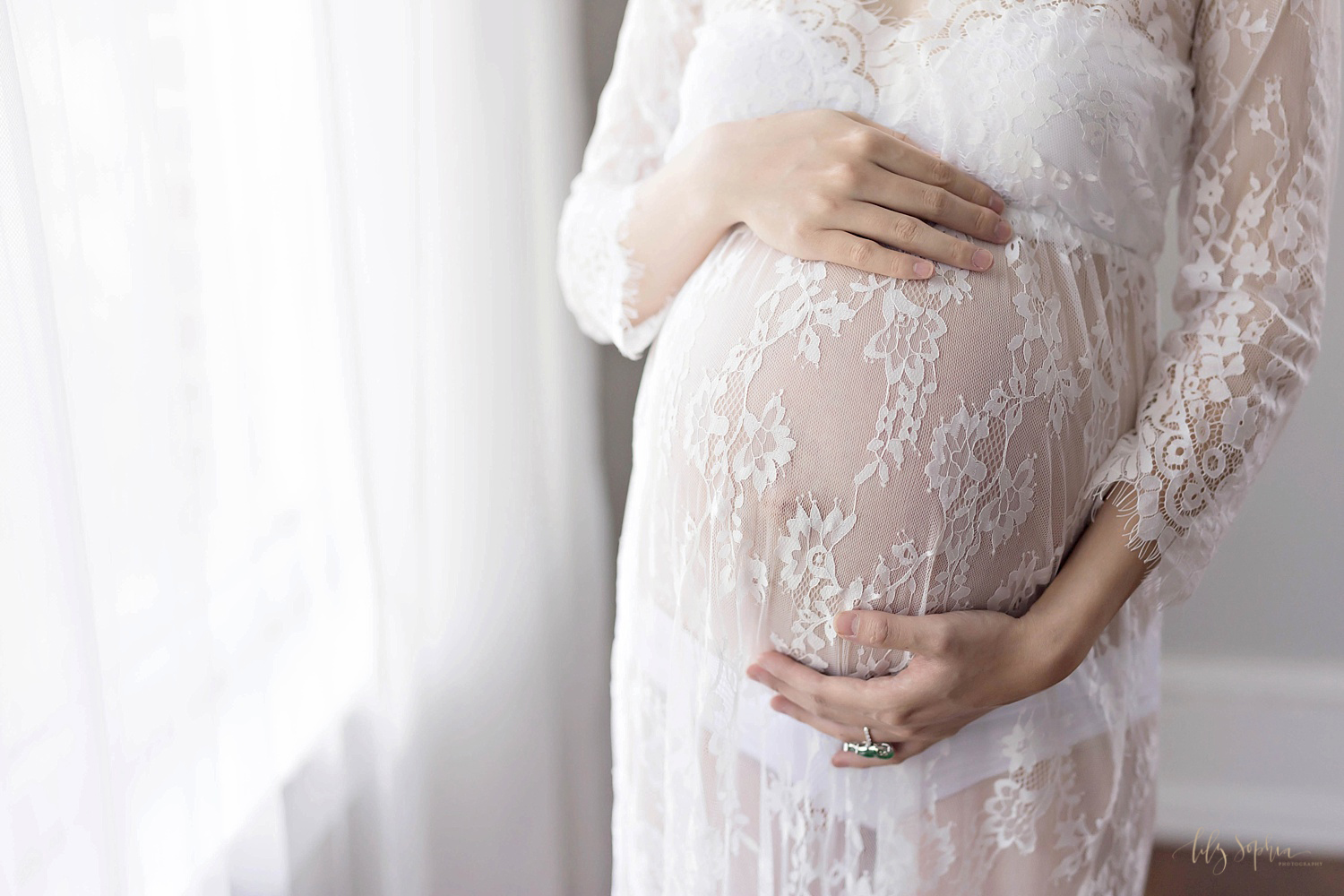  Image of pregnant woman's belly dressed in a white sheer lace dress taken in a natural light studio in Atlanta.&nbsp; 