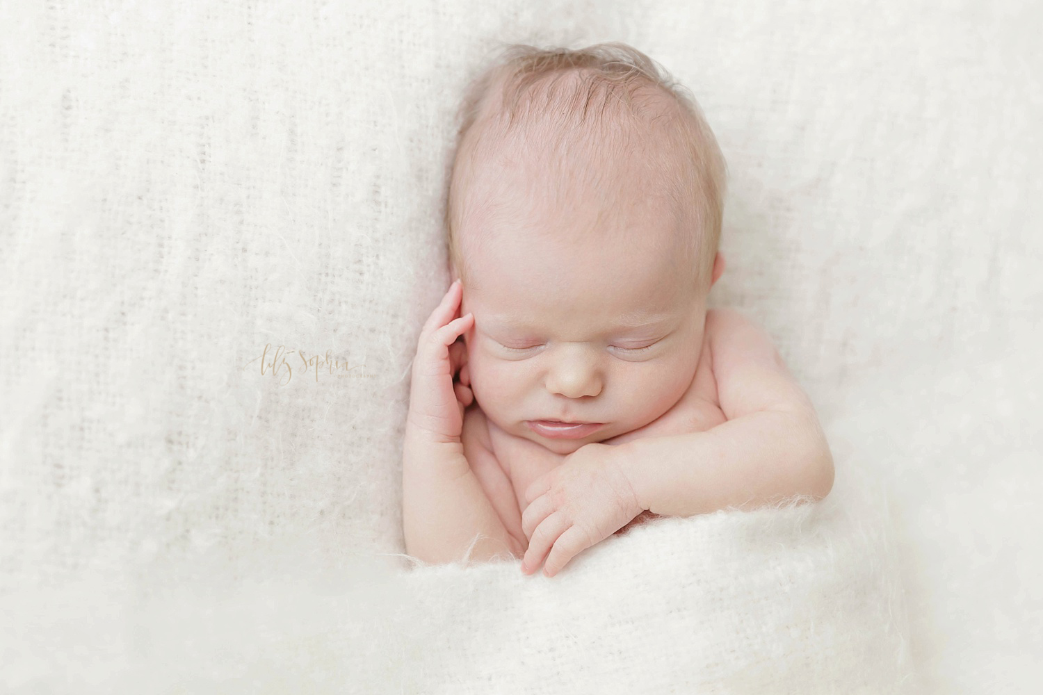 Sleeping newborn baby girl on white blanket with hand on cheek in natural light studio of Lily Sophia Photography located in Atlanta, Georgia