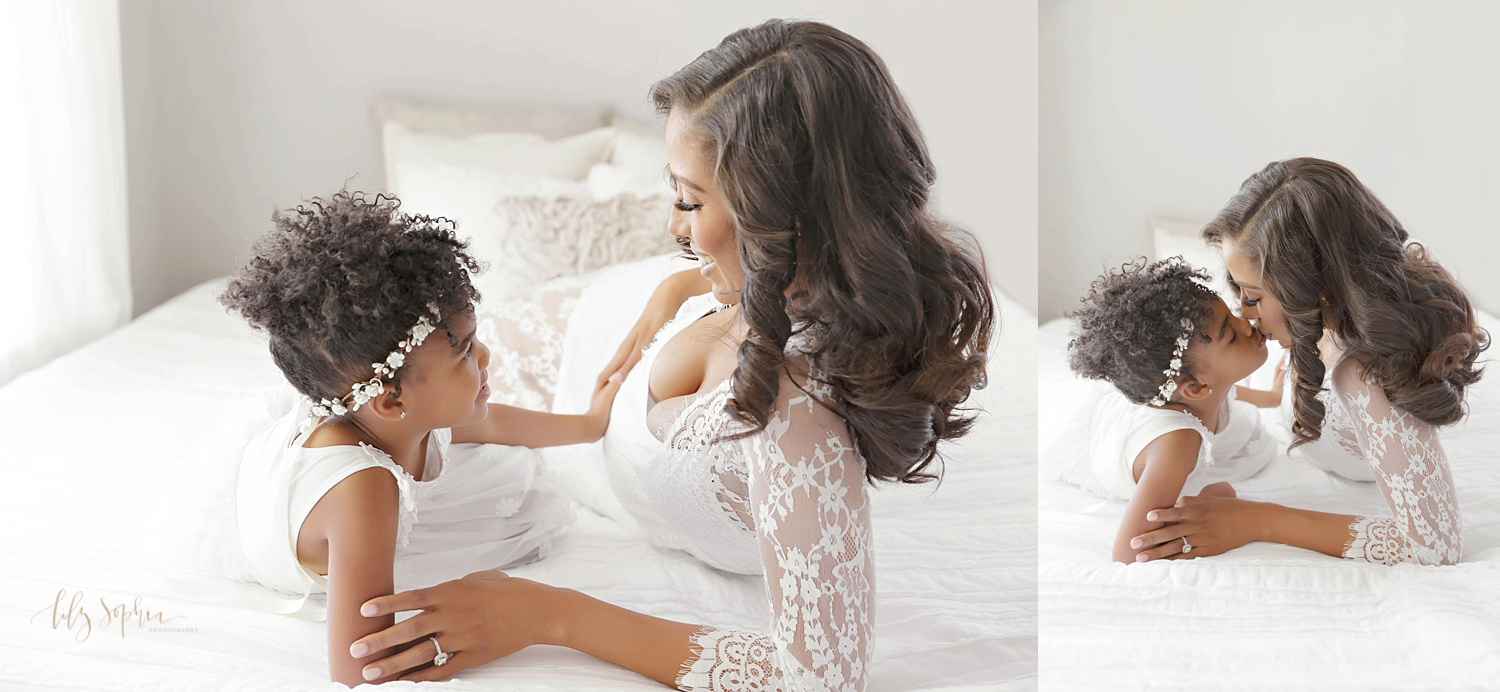 Pregnant black woman in white lace dress kissing little girl niece on bed in natural light studio in Atlanta