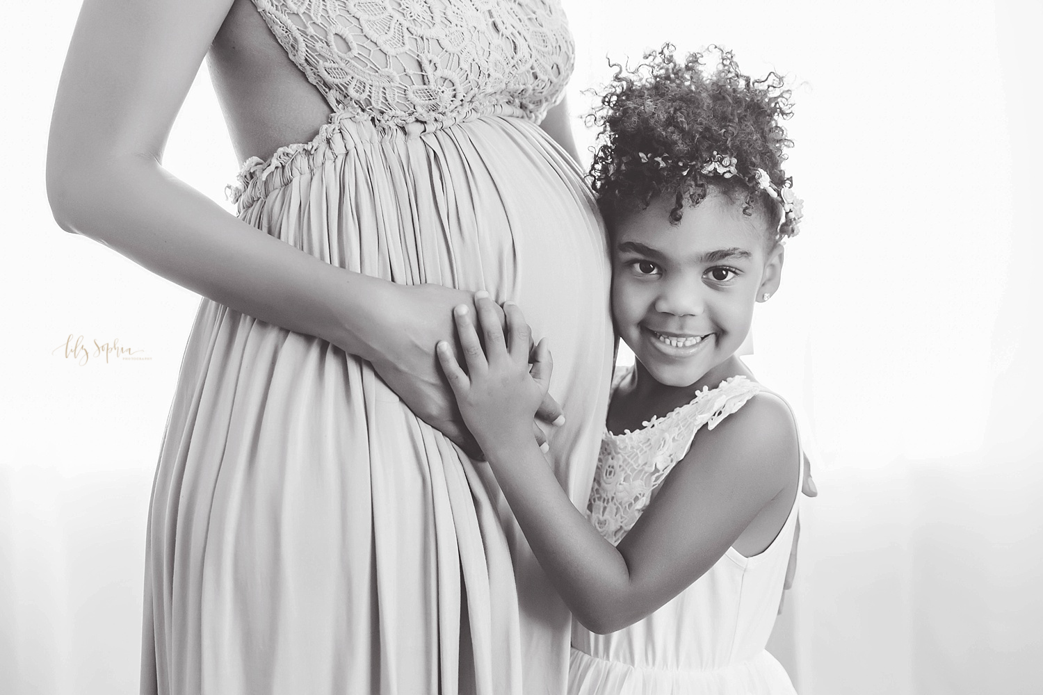 Black and white image of happy little girl hugging her aunt's pregnant belly in natural light studio located in Atlanta