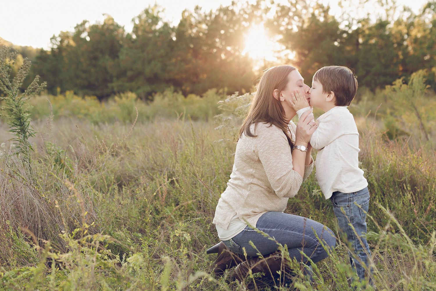  A little boy holds his mother's face to give her a kiss with the sunset behind them. Image taken during a family portrait session by Lily Sophia Photography of Atlanta in the field location.&nbsp; 