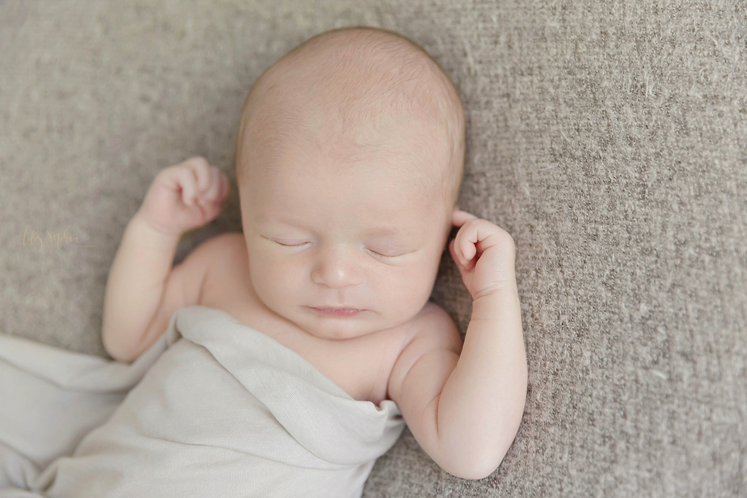  Sleeping, newborn boy in a gray wrap with his hands by his head.&nbsp; 