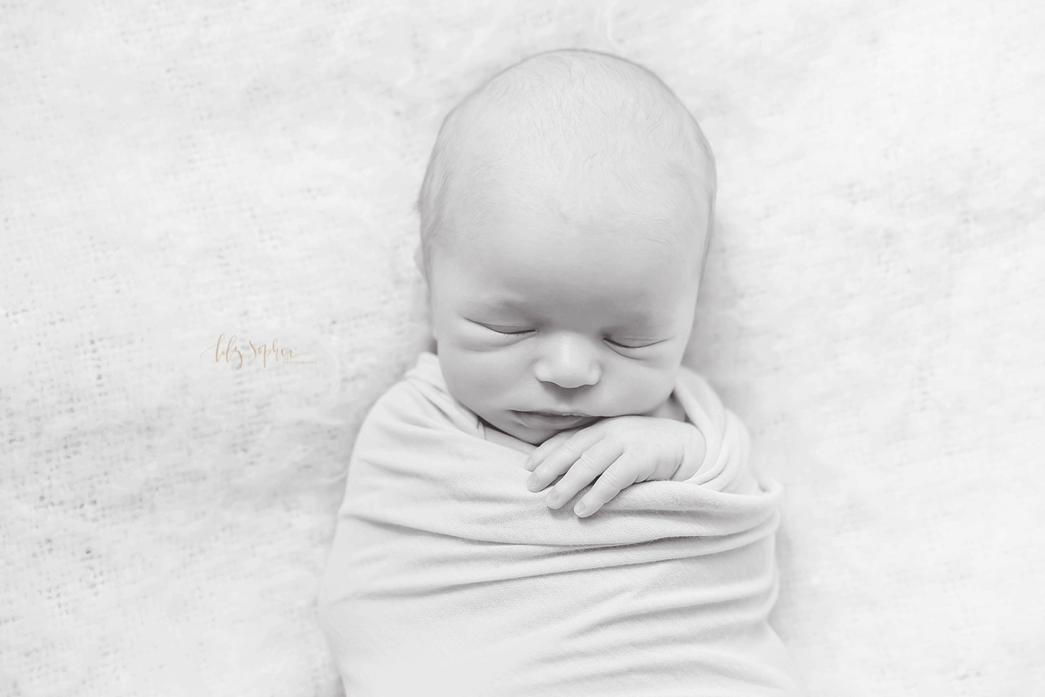  Black and white image of a sleeping, newborn, boy, wrapped in a wrap with one hand peeking out.&nbsp; 