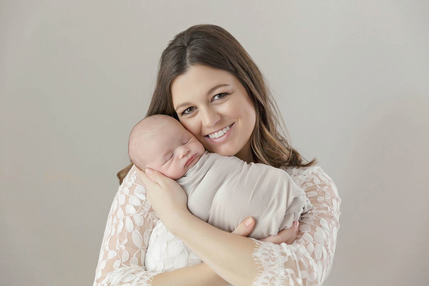  A mother holding up her sleeping, newborn, boy, smiling at the camera.&nbsp; 