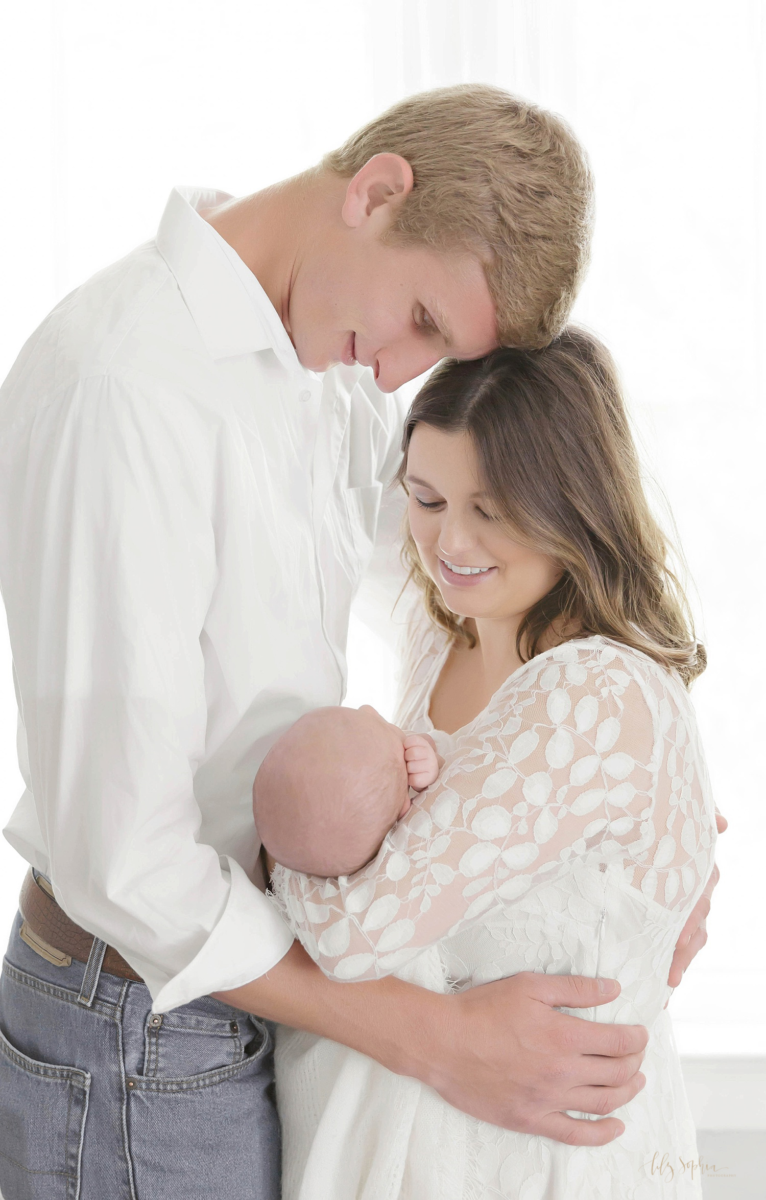  Image of parents facing each other, while they hold their sleeping, newborn son in their arms.&nbsp; 