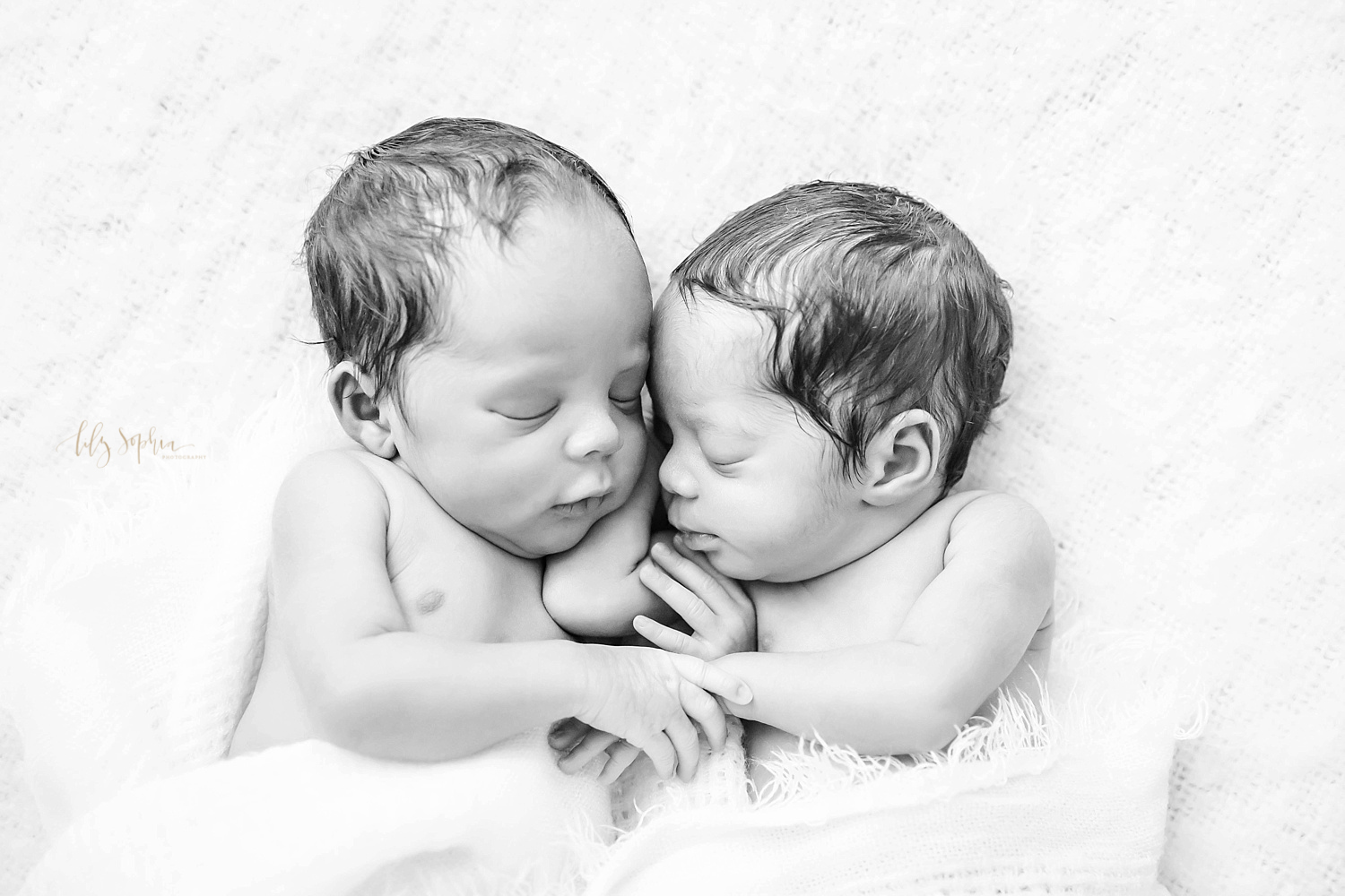  Black and white image of sleeping, African American, newborn twins cuddled up together, holding hands. &nbsp; 