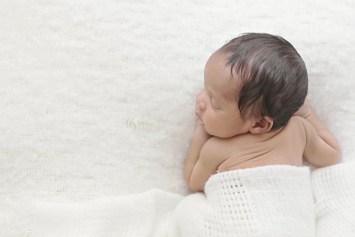  Image of an African American newborn boy, sleeping on his stomach with a white blanket covering him. 
