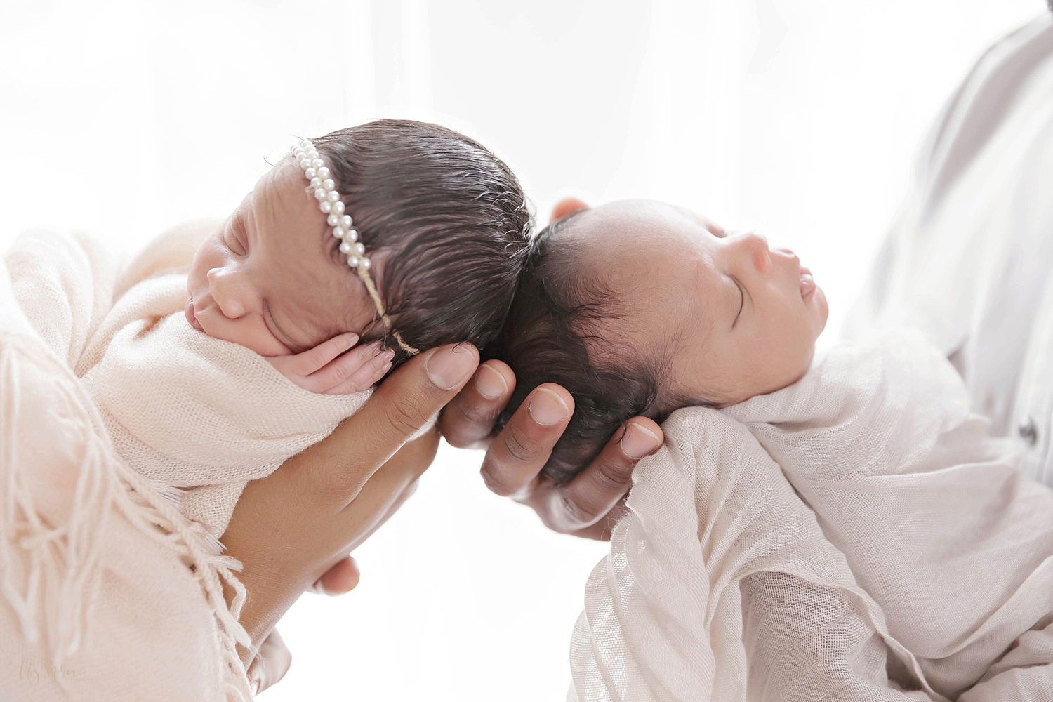  Image of sleeping, African American, newborn twins being held up head to head and wrapped in blankets. 