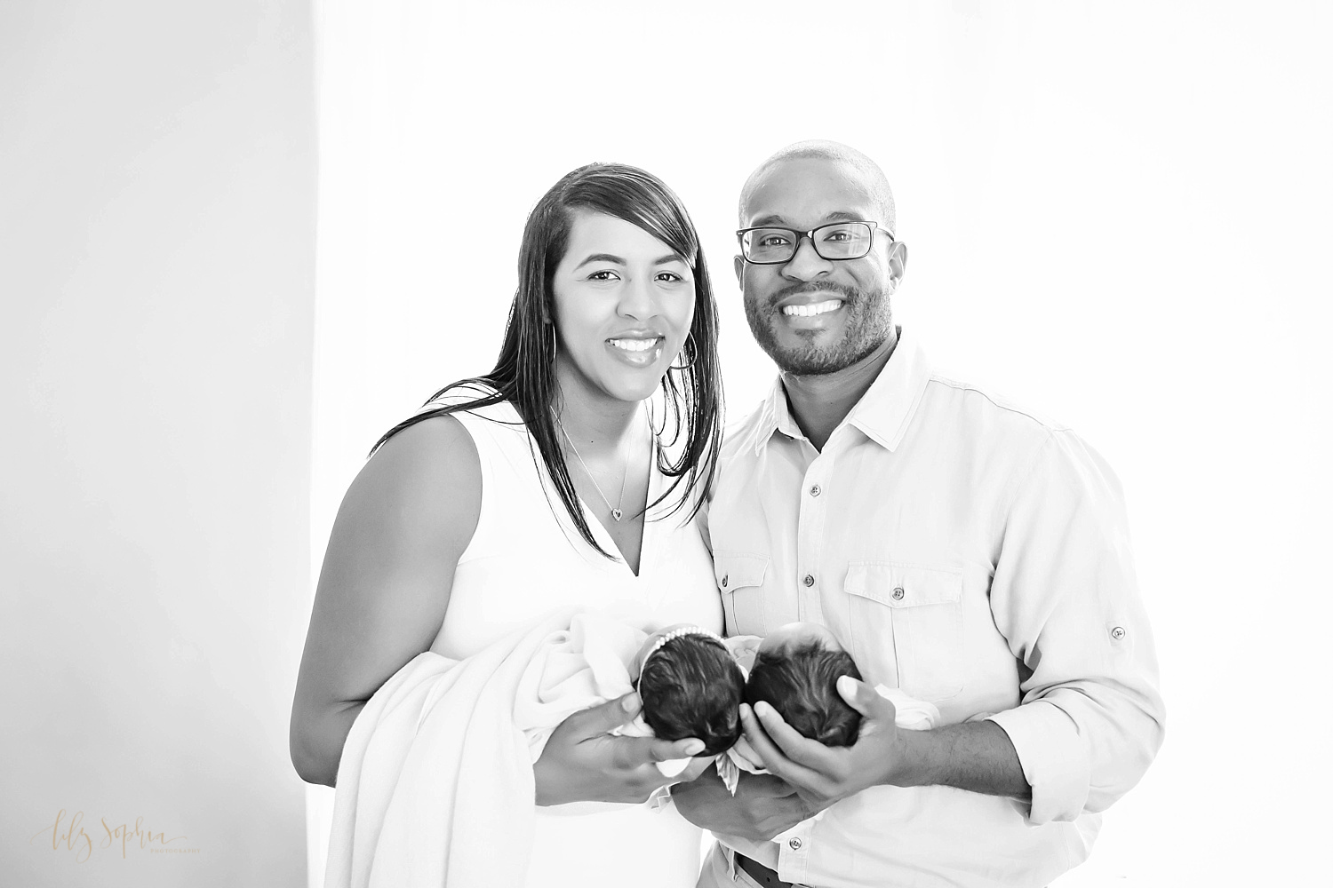  Black and white image of an African American mom and dad holding their newborn boy/girl twins and smiling at the camera. 