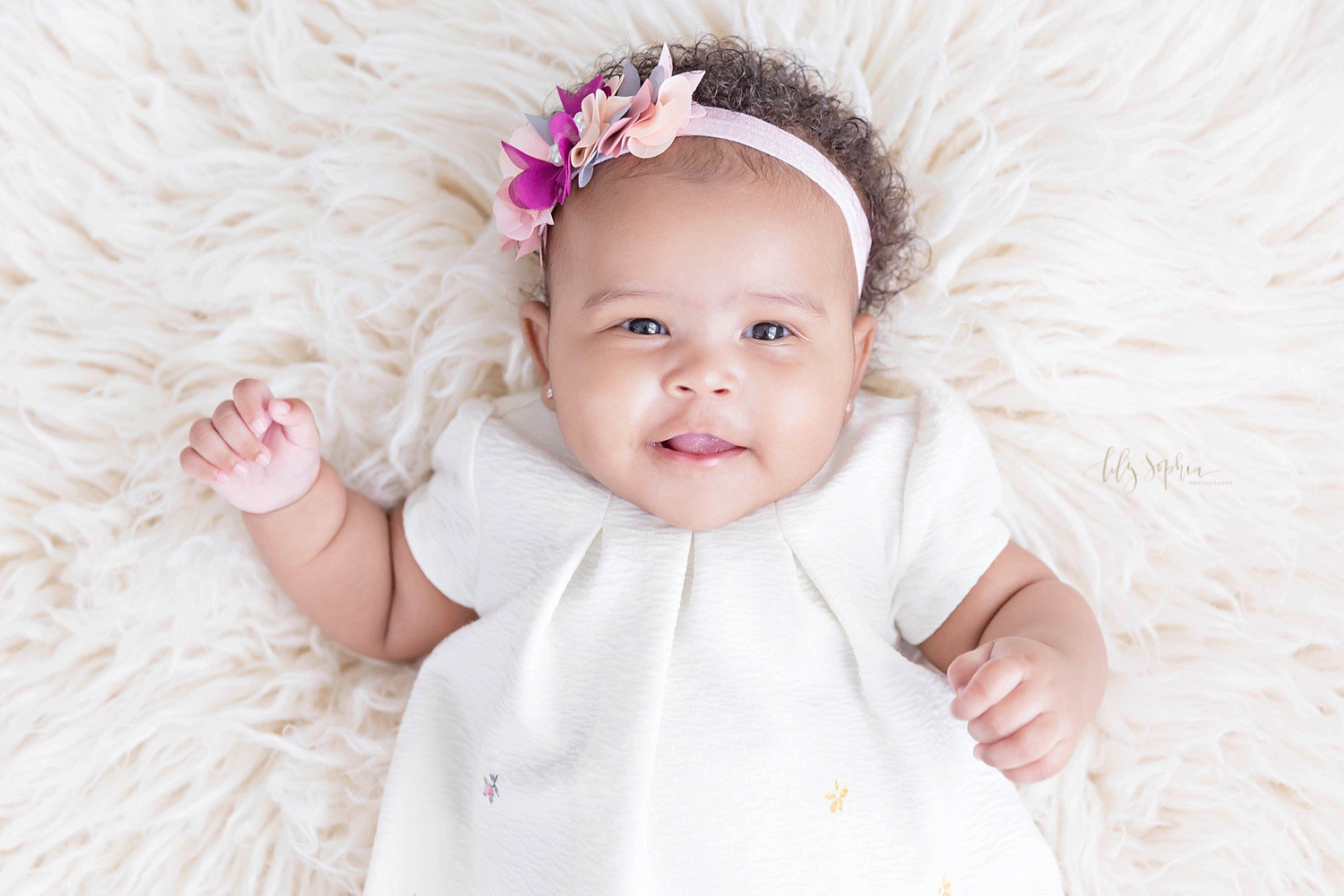  Image of an African American, three month old, baby, girl, laying on a cream flokati and smiling.&nbsp; 