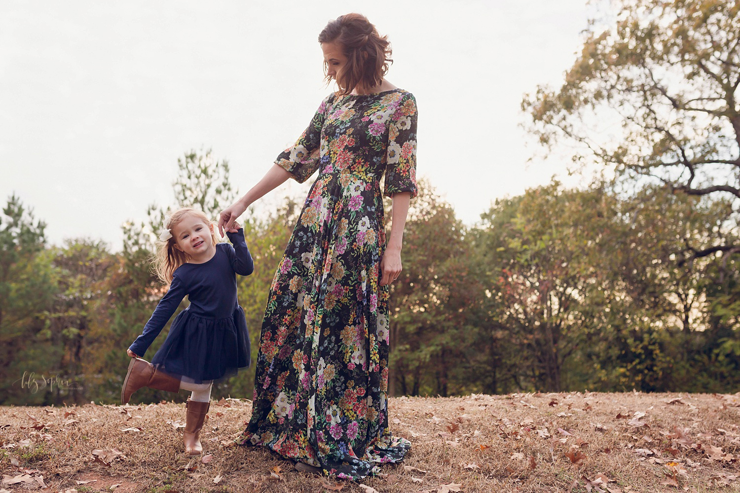  A little girl in a navy dress with brown boots dances with her mother who is wearing a floral maxi dress. Taken by Lily Sophia Photography in Atlanta, GA. 