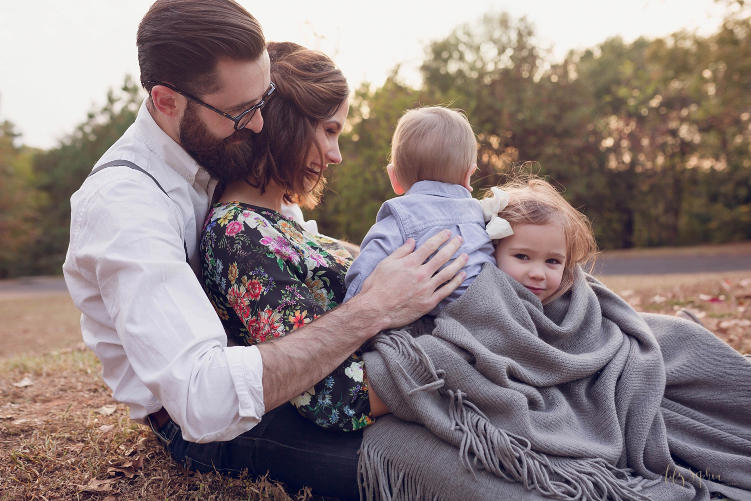  A mother, father, baby boy, and toddler girl sitting on a blanket close together and interacting naturally at sunset in Atlanta.&nbsp; 