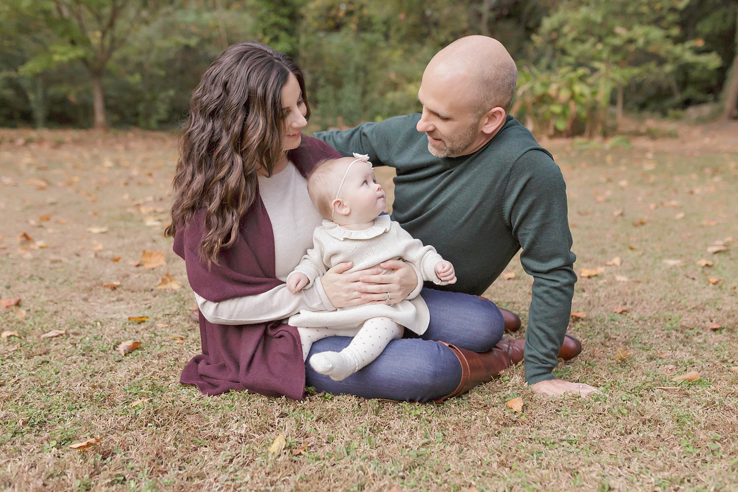  Image of family sitting on the grass with fall leaves around them in the garden location of Lily Sophia Photography. 