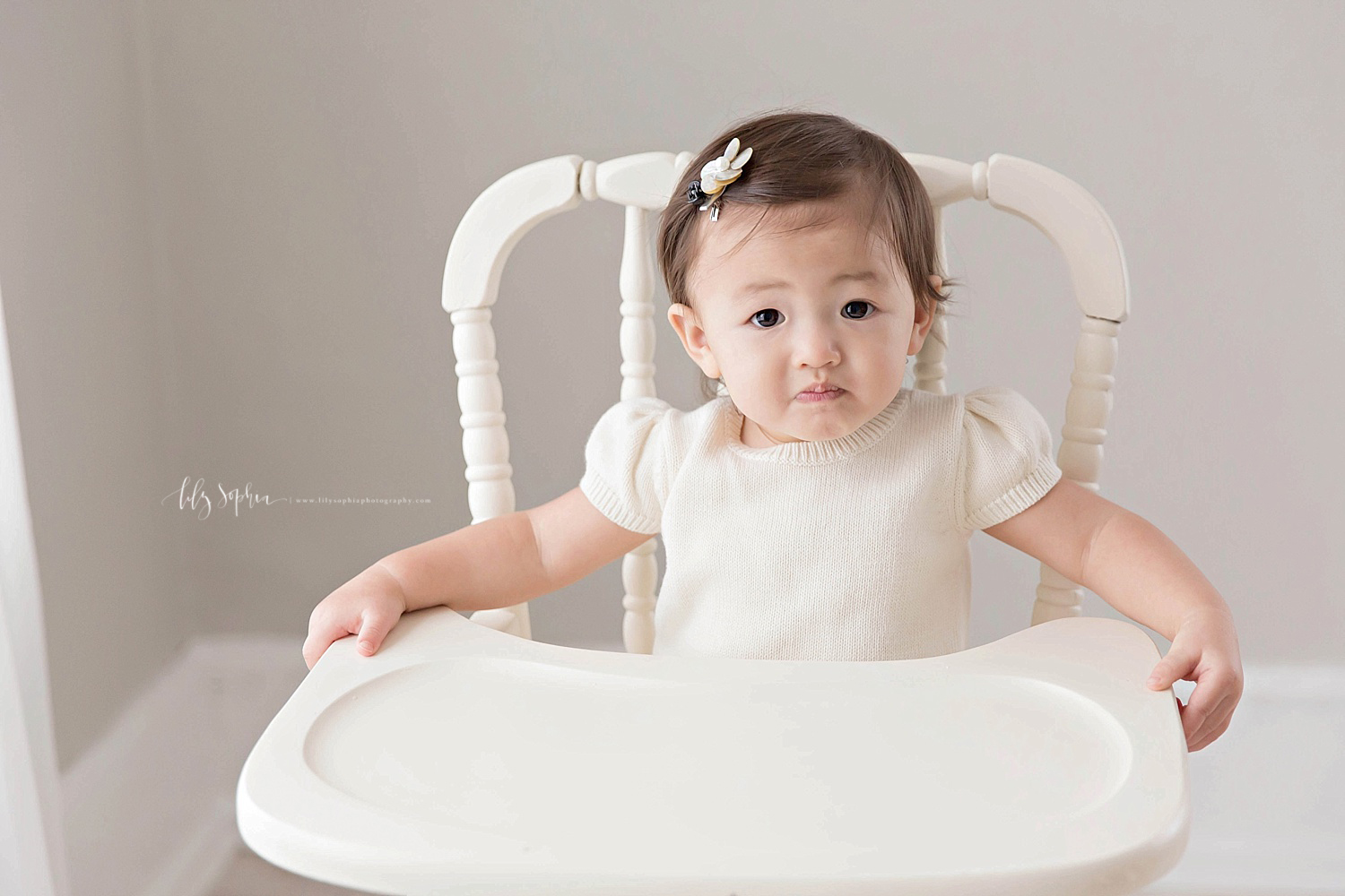 Image of an Asian, baby, girl, sitting in an antique wooden, high chair. 