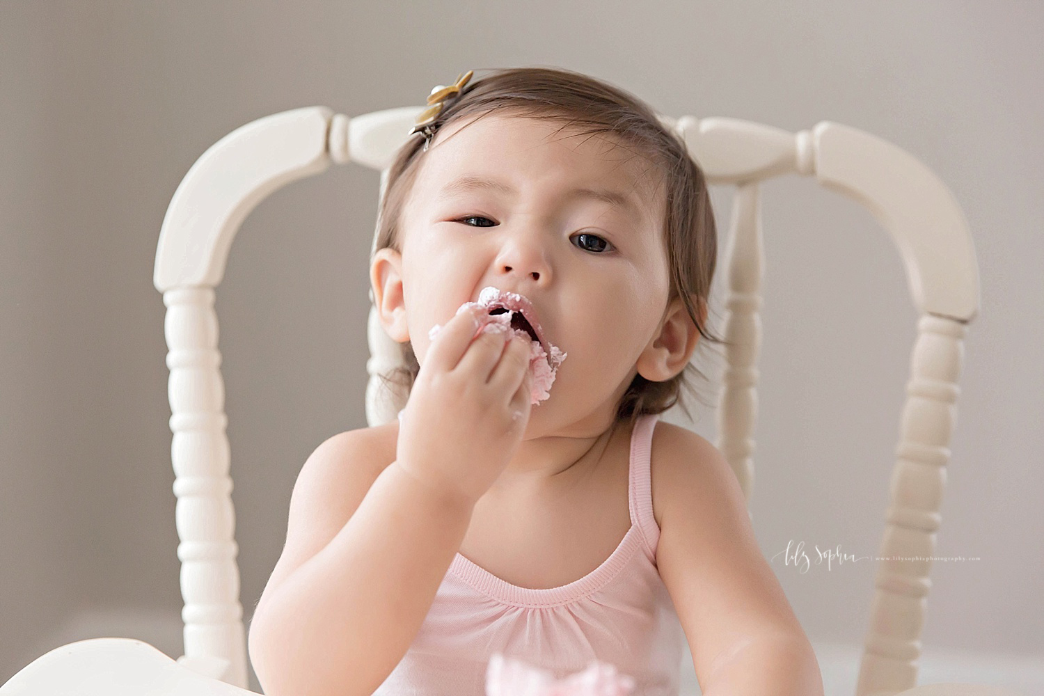  Image of an Asian, baby, girl, stuffing her icing covered fingers into her mouth.&nbsp; 