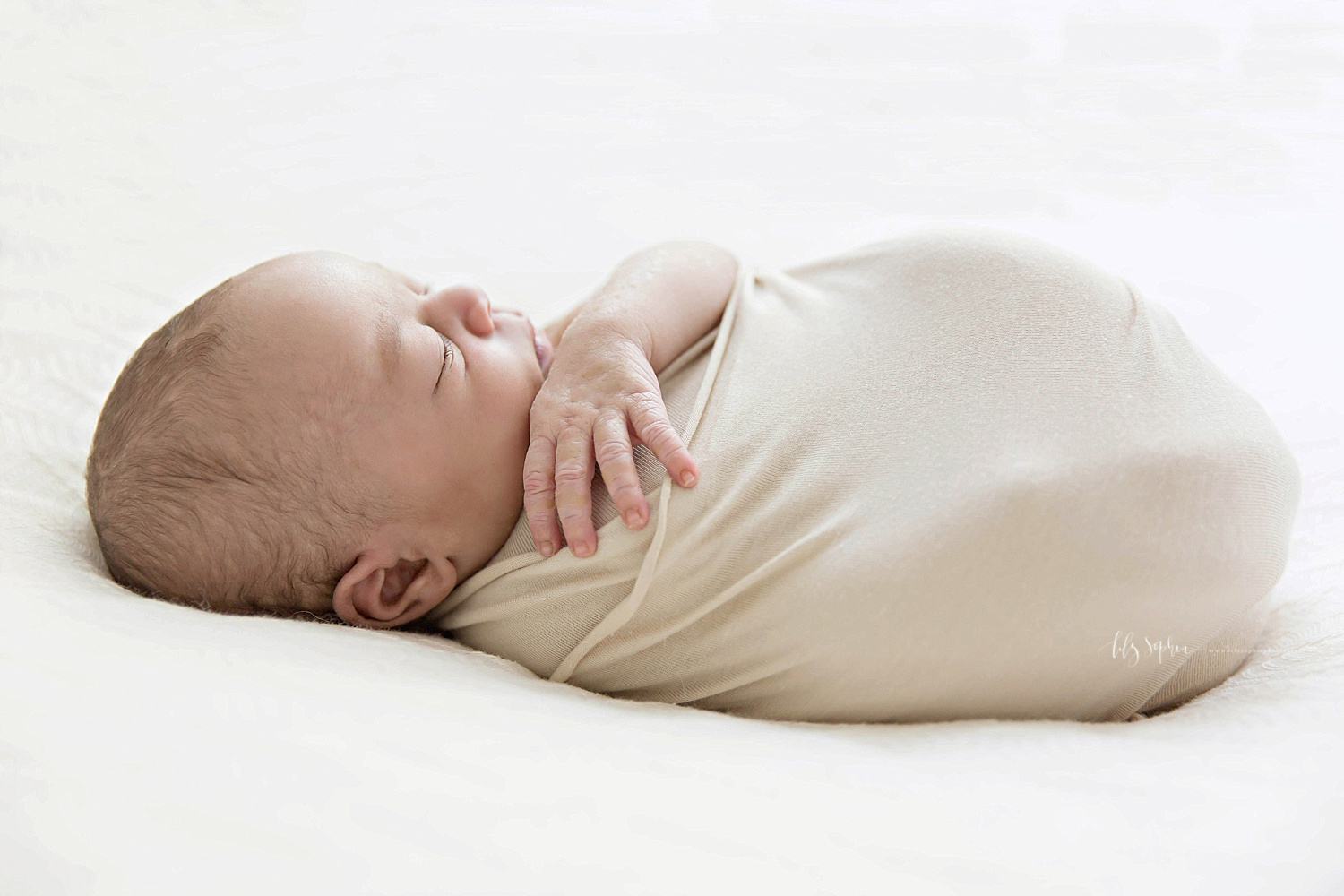  Image of a sleeping, newborn, African American, baby, boy, wrapped in a tan blanket, with one arm sticking out.&nbsp; 