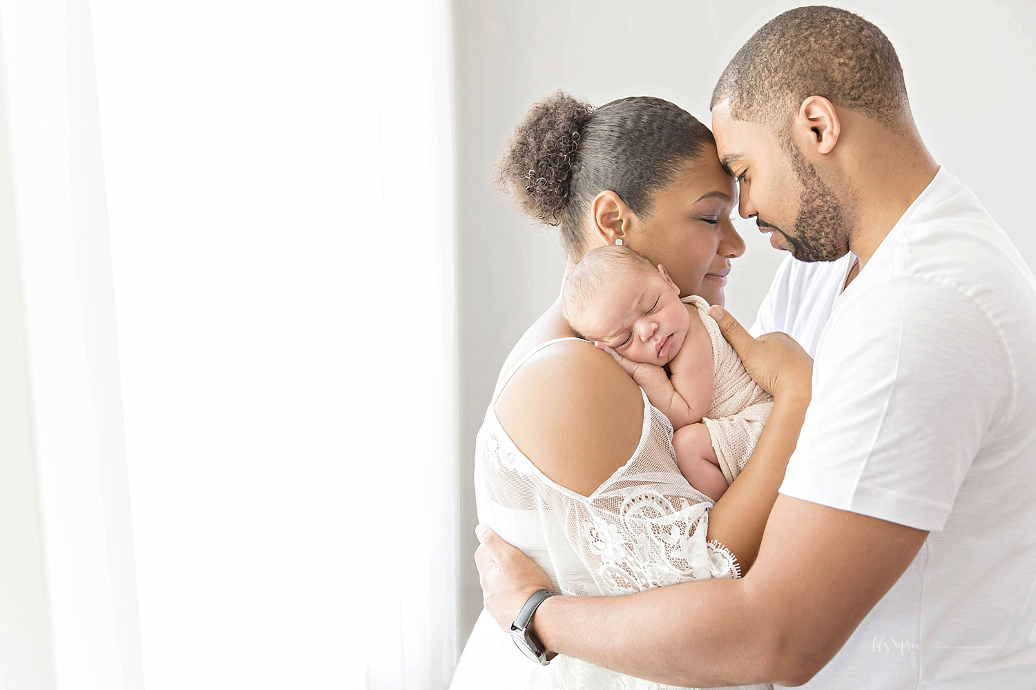  Image of an African American couple, forehead to forehead, with their sleeping newborn, son, laying on his mother's shoulder.&nbsp; 