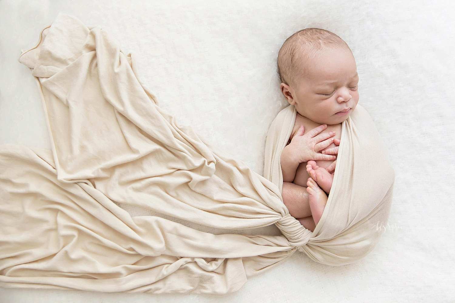  Image of a sleeping, newborn, African American, boy, curled up in a tan wrap, with his fingers and toes on his chest.&nbsp; 