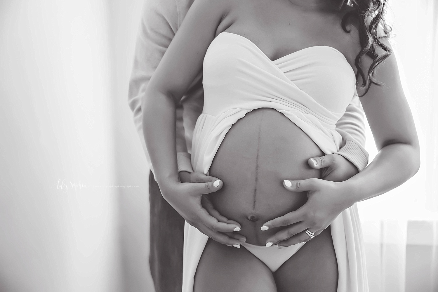  Black and white close up image of an pregnant, African American, woman's belly, with her and her husband's hands on it.&nbsp; 