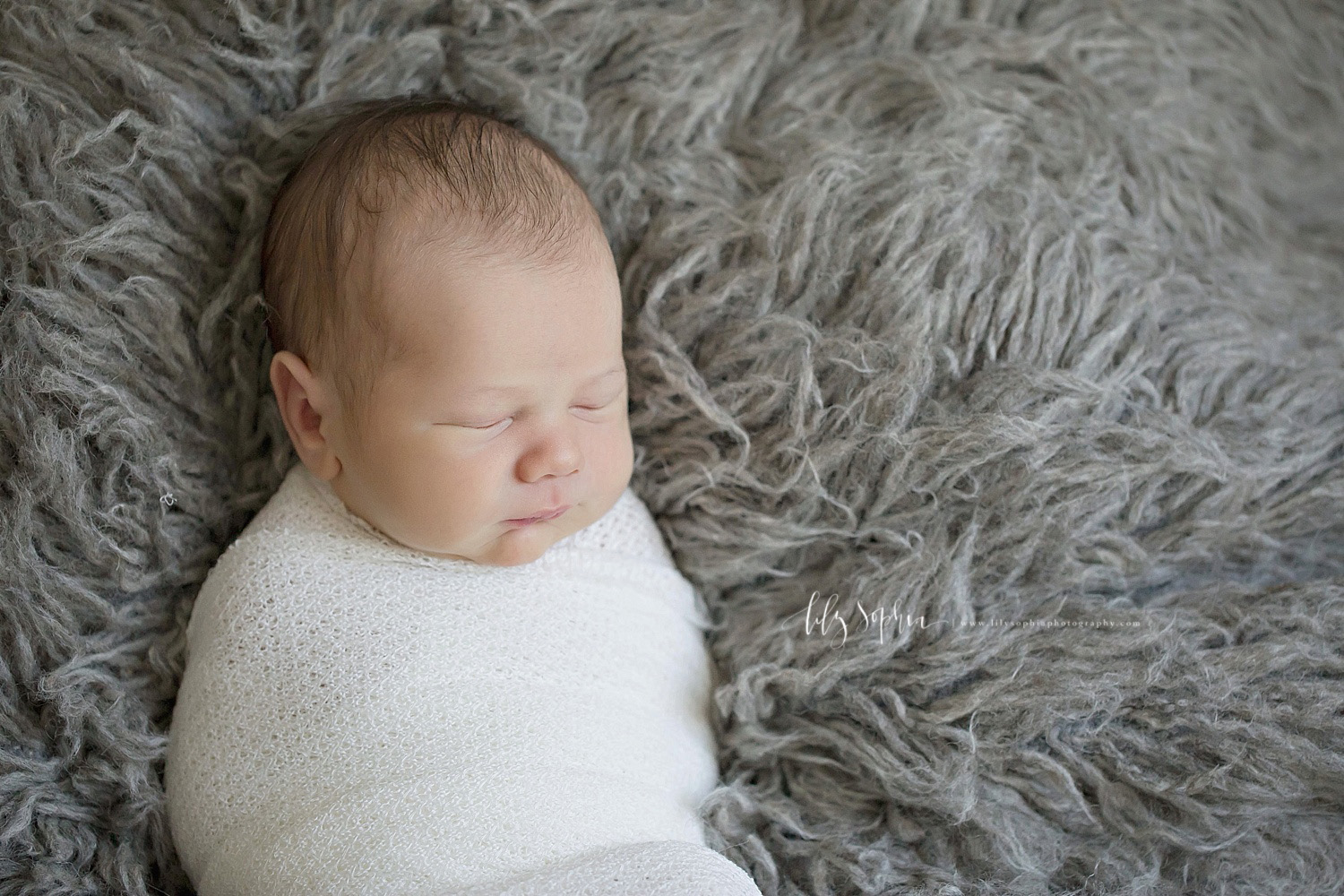  Image of a sleeping, newborn, baby, boy, wrapped up in a white blanket and laying on a gray flokati,.&nbsp; 