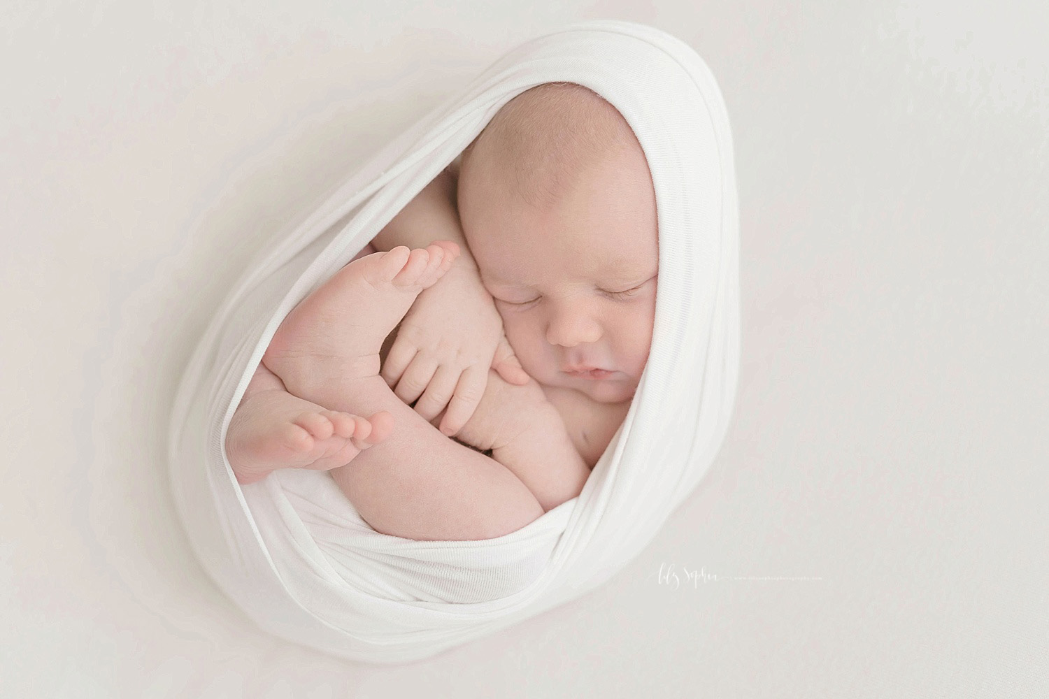  Image of a sleeping, newborn, boy, wrapped up in a white blanket in the egg pose.&nbsp; 