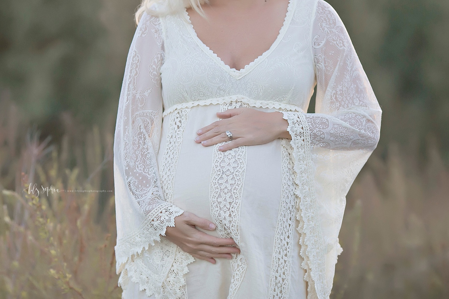  Image of a pregnant woman, with one hand on top of her belly and the other below it, standing in a field at sunset.&nbsp; 