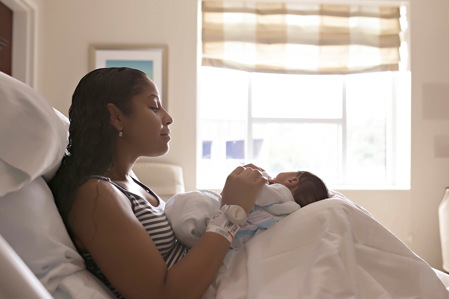 Image of an African American woman, sitting in a hospital bed with playing with her newborn, baby, son.&nbsp; 