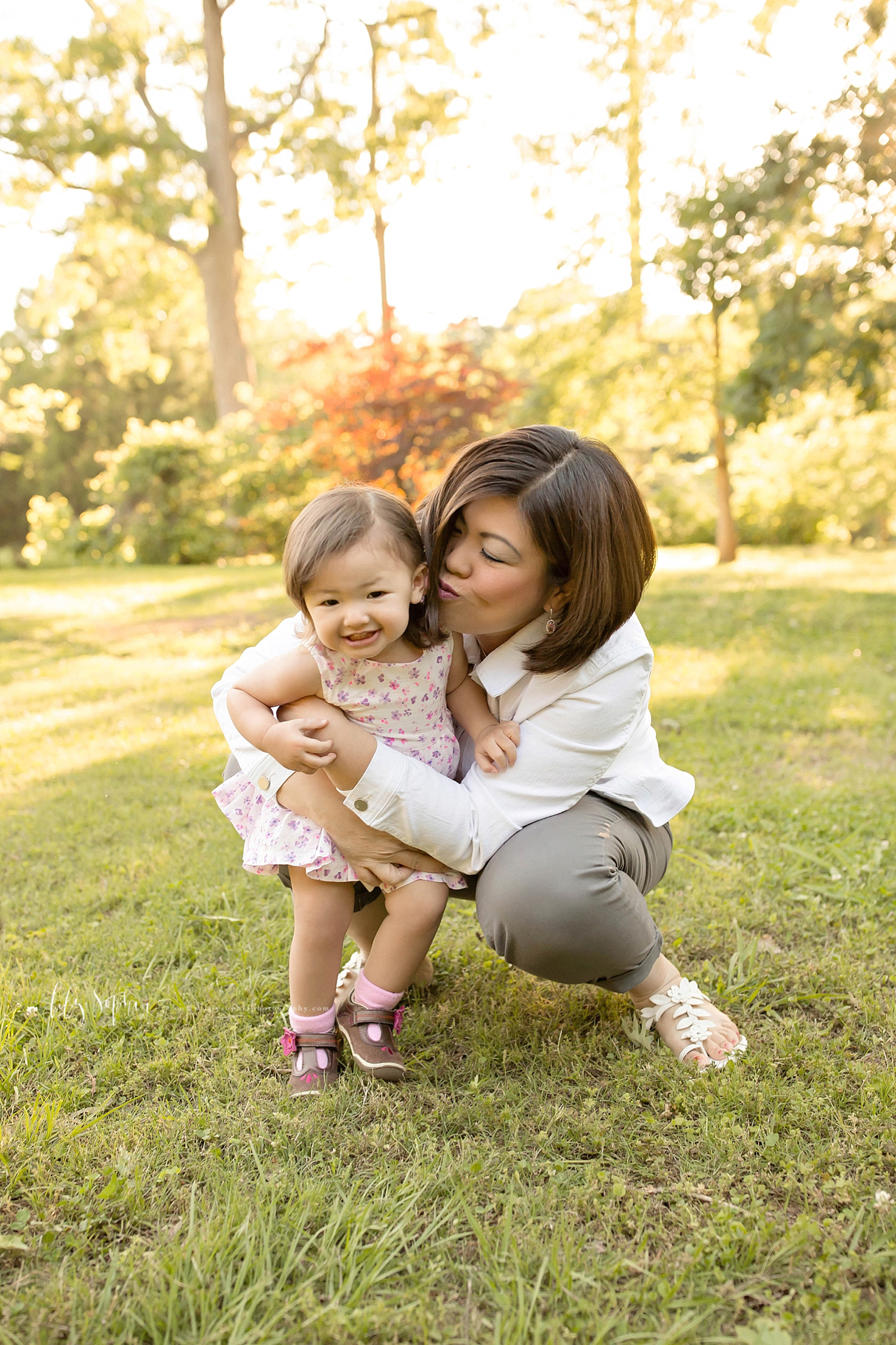  Image of an Asian mother kissing and hugging her little daughter, in a park.&nbsp; 