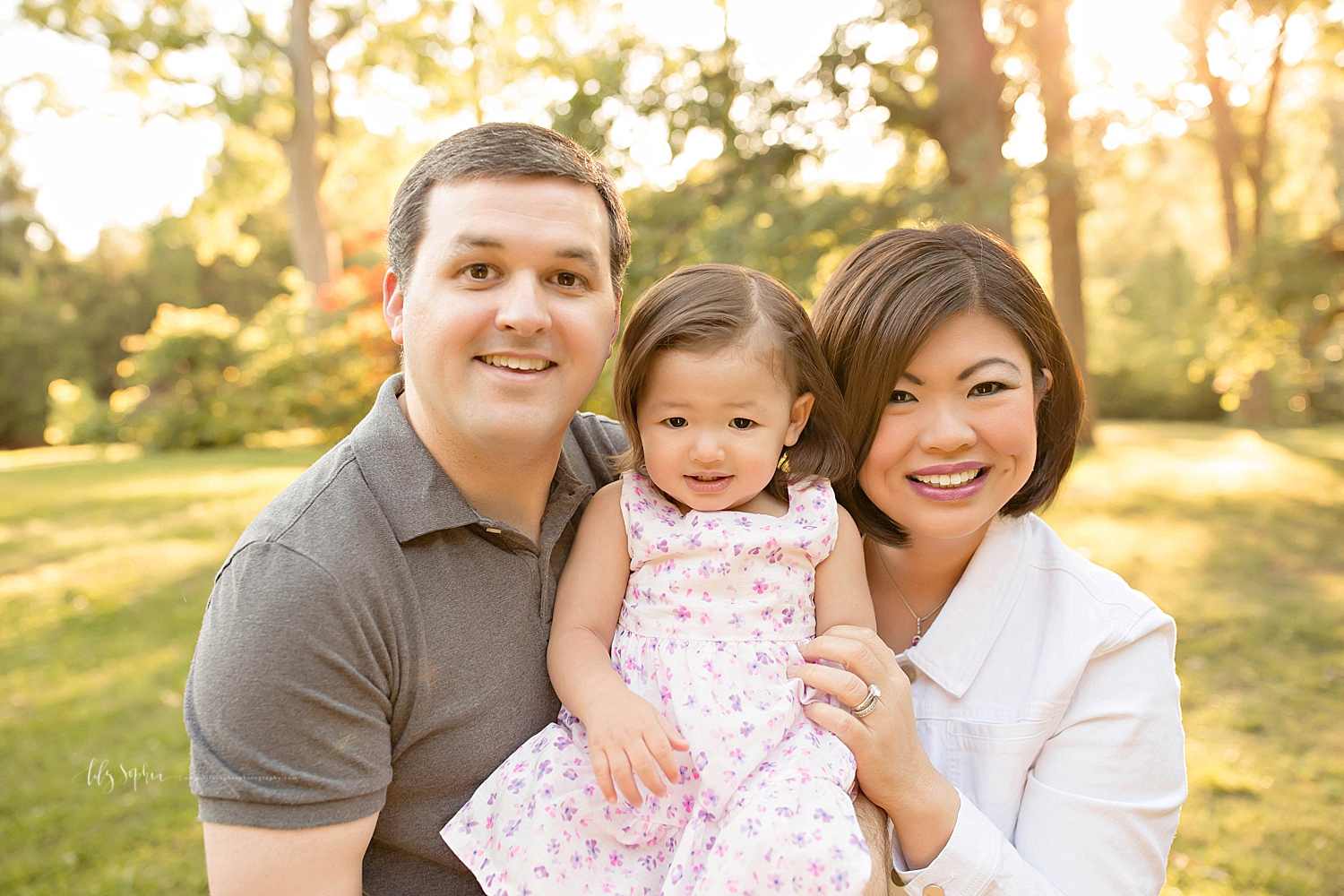  Image of a man, his daughter, and his Asian wife, smiling at the camera, in a park.&nbsp; 