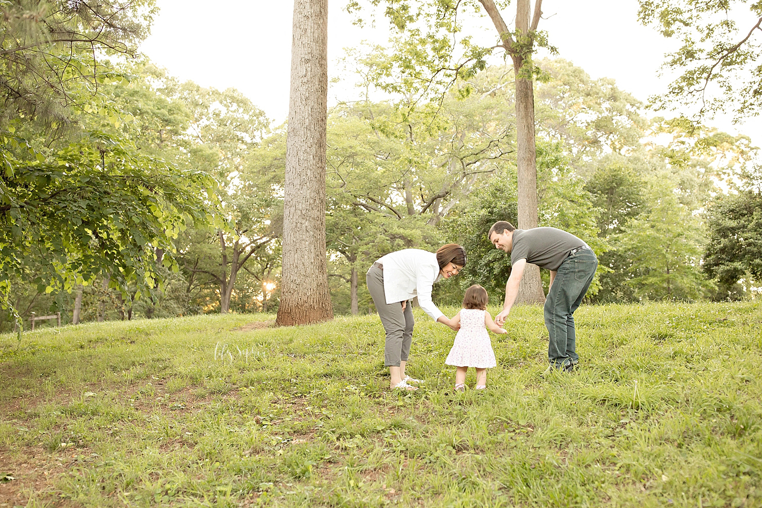  Image of a man and his Asian wife, holding their daughters hand's, as she stands between them in a park.&nbsp; 