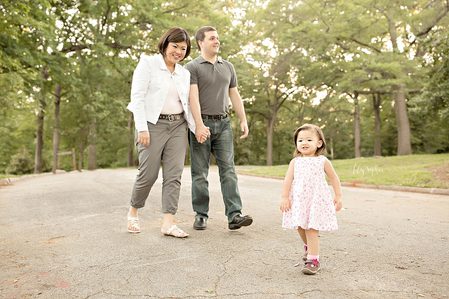  Image of a man and his Asian wife, holding hands, smiling at, and walking behind their little daughter.&nbsp; 